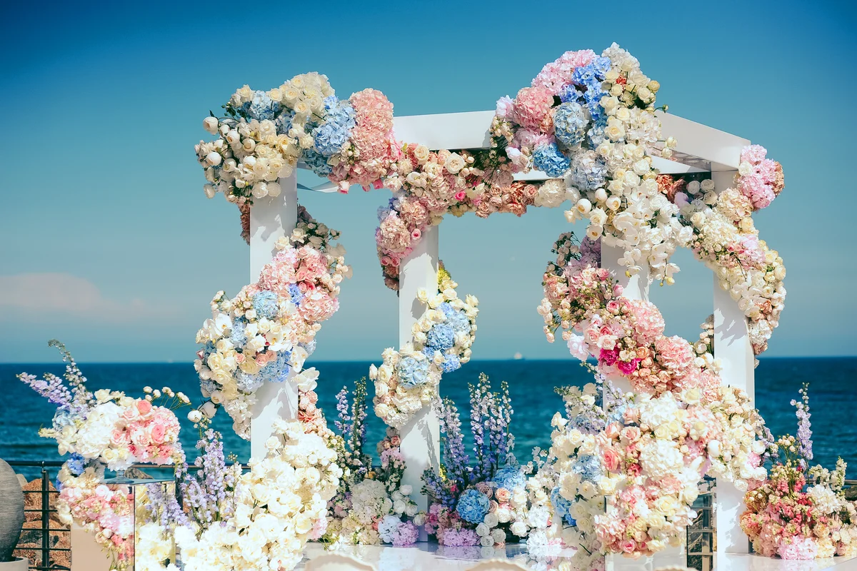 Florália: A Escolha dos Decoradores de Eventos. Arco floral com hydrangeas, rosas e flores em tons pastel para cerimónia de casamento junto ao mar.