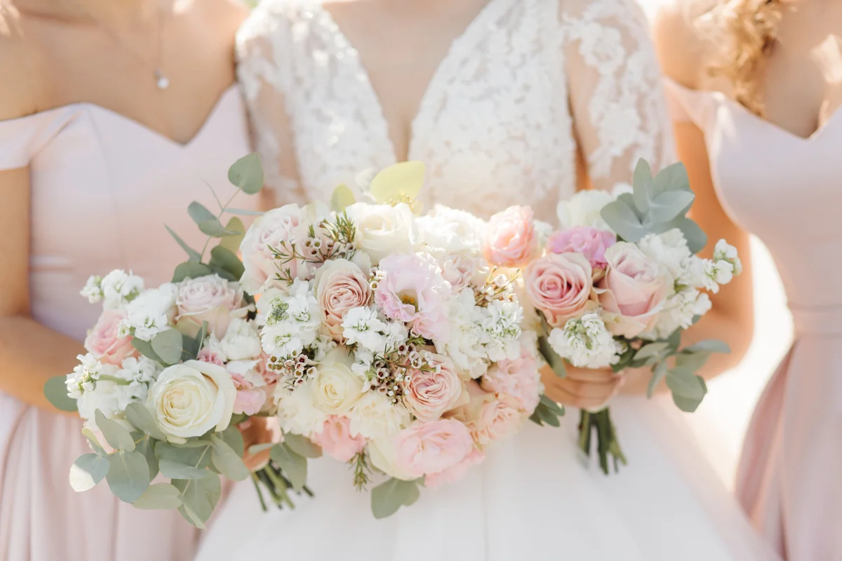 Flores Grossistas para Ramos de Noiva e Arranjos Exclusivos. Noiva e damas de honor com bouquets de rosas brancas e rosa suave para casamento elegante.
